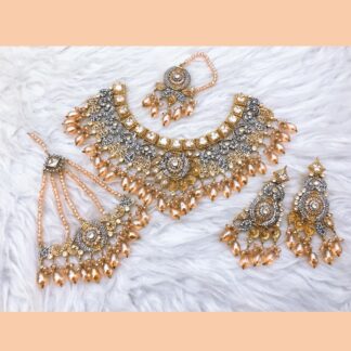 A luxurious gold-plated Kundan necklace set with green emerald beads, intricate polki stones, matching earrings, a maang tikka, and a passa, displayed on a soft fabric background.