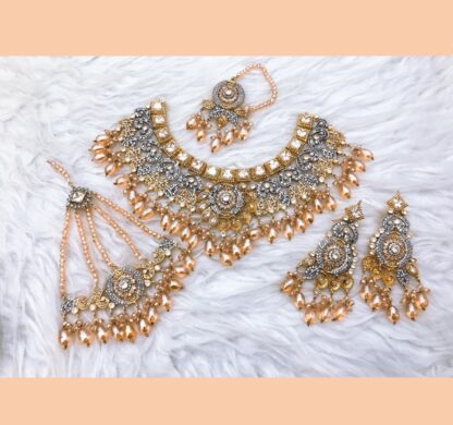 A luxurious gold-plated Kundan necklace set with green emerald beads, intricate polki stones, matching earrings, a maang tikka, and a passa, displayed on a soft fabric background.