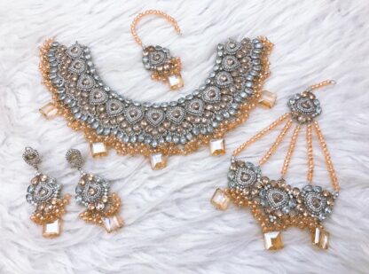 Elegant Kundan choker set in silver and peach tones, featuring intricate stonework, bead detailing, matching earrings, maang tikka, and hand jewelry.