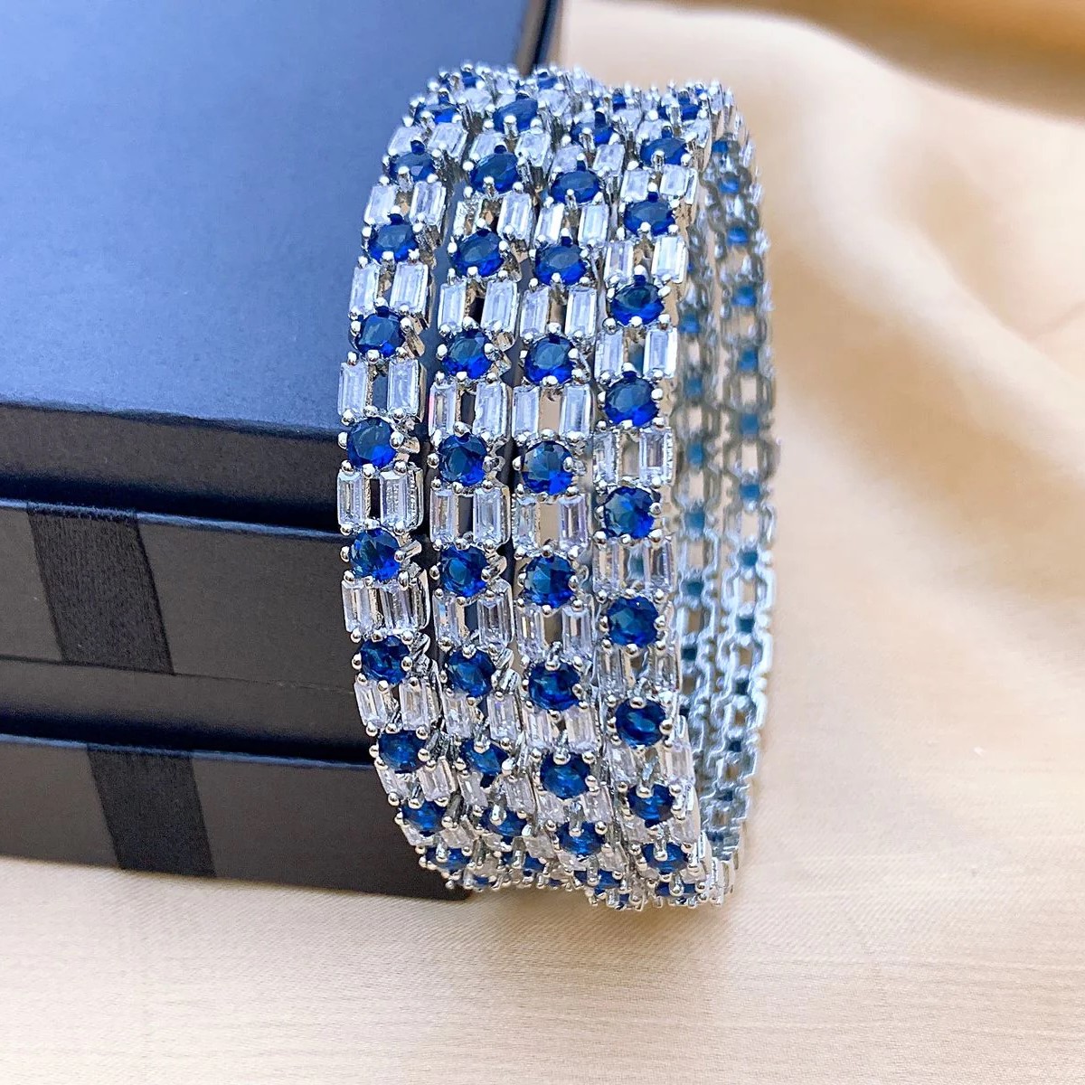 Rhodium Plated American Diamond Bangles with Blue Sapphire Stones Detailed close-up of rhodium plated American diamond bangles showcasing blue gemstones and intricate CZ stone pattern by Carat Vogue