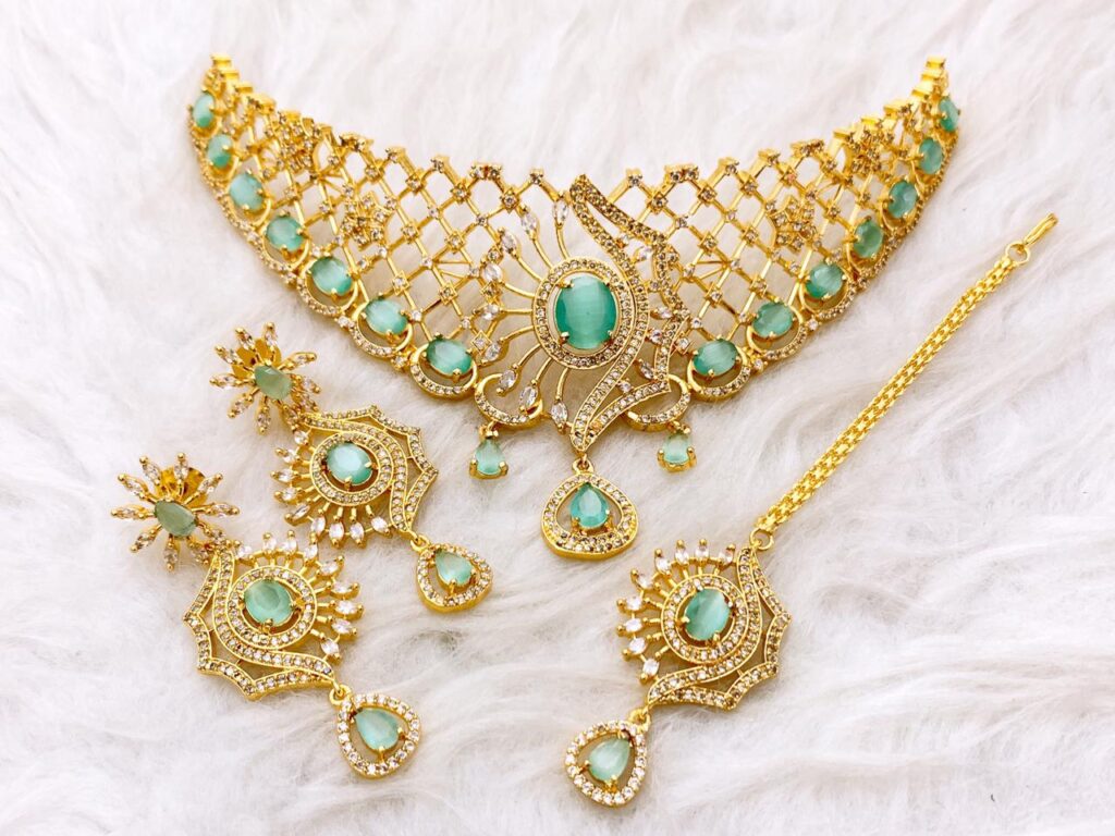 Heavy Gold Plated Bridal Choker Set with large Mint Green Zumarad color stones in a sunburst design. Includes matching heavy earrings and a Maang Tikka. Traditional look for Baraat or formal wedding wear.