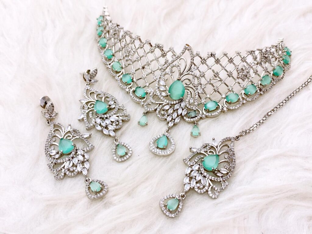 Silver Rhodium Plated AD Choker Set for Pakistani Bride. Features Mint Green oval stones, clear Zircon American Diamonds, dangling drops, and matching earrings with a Maang Tikka. Ideal for Walima or Nikkah.