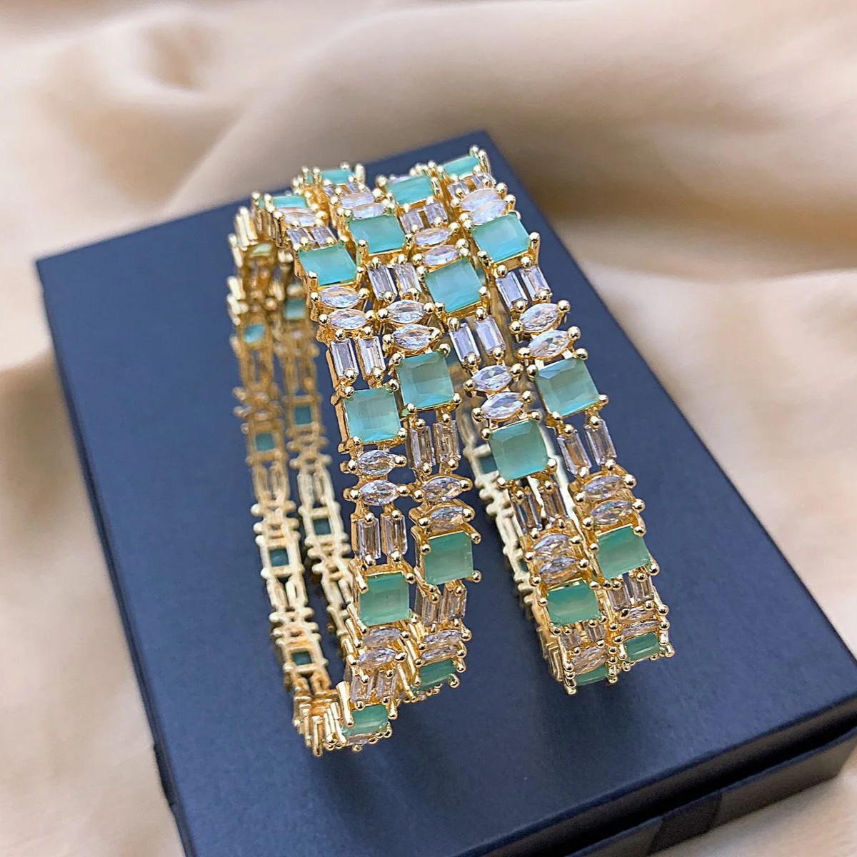 Mint Green AD Bangles (Set of 4) Styled presentation of gold bangles with mint green stones placed on a ribboned box, ideal for bridal, Eid, or formal wear promotions.