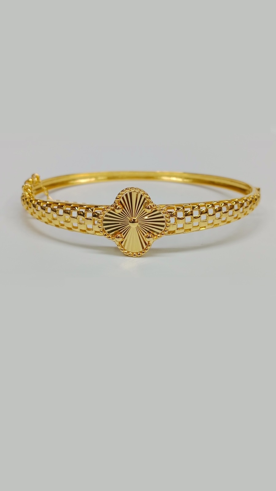 Luxury 22ct Gold Bangle Collection: Clover Designs and Intricate Finishes Stylish 13.100 Grams gold bangle with a sunburst clover centerpiece and a contemporary, repeating square-link pattern forming the entire band.