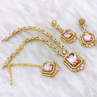 4-piece peach champagne jewelry set featuring a gold-plated necklace, earrings, and maang tikka on a white faux fur background.