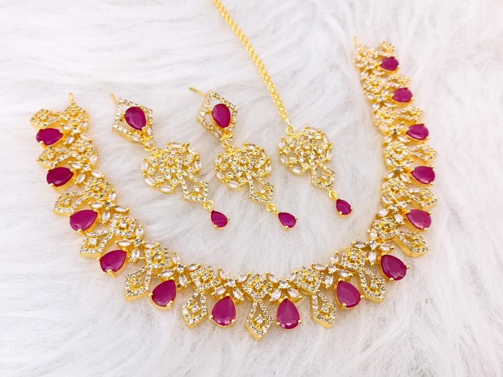 Ruby Red Teardrop Gold-Plated Jewelry Set Traditional ruby red and gold jewelry set with fringe necklace, earrings, and maang tikka.