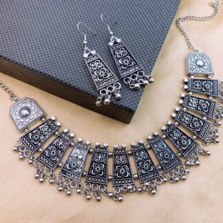 Chrome Hearts Inspired Oxidized Silver Tribal Sets | HK Gothic Style Tribal style oxidized silver bib necklace and earrings set featuring floral engraved trapezoidal plates and rhythmic metallic ghungroo bell fringe charms.