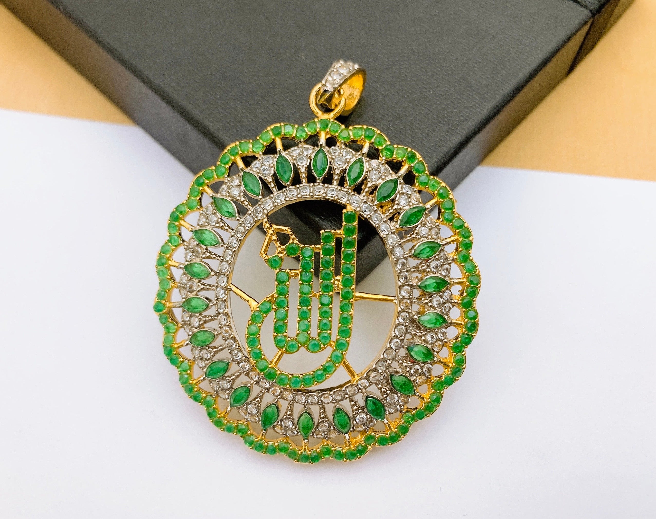 Divine Emerald Green Allah Calligraphy Pendant with Diamond Accents A divine emerald green Allah calligraphy pendant showcasing a circular design with marquise-cut green stones and shimmering American Diamond accents in a gold frame.