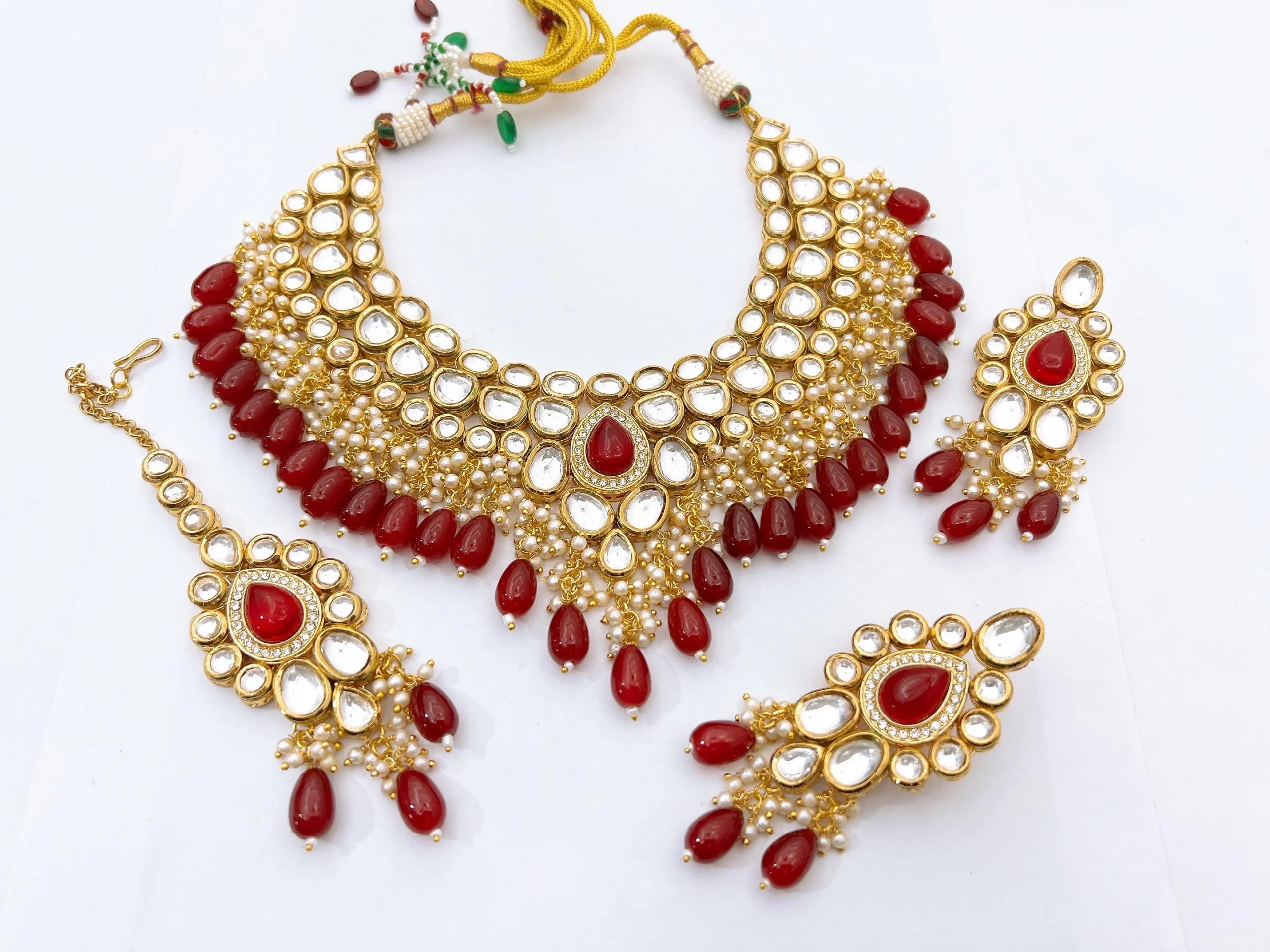 Royal Ruby Red Kundan Bridal Choker Set with Matching Earrings & Maang Tikka Grand ruby red Kundan bridal choker necklace with teardrop red beads, matching earrings, and maang tikka on a white background.