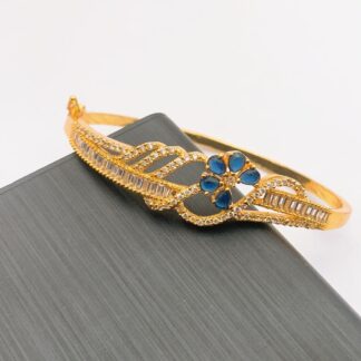 Gold-tone bangle featuring a single sapphire blue crystal flower and a wave of baguette and round American Diamonds.
