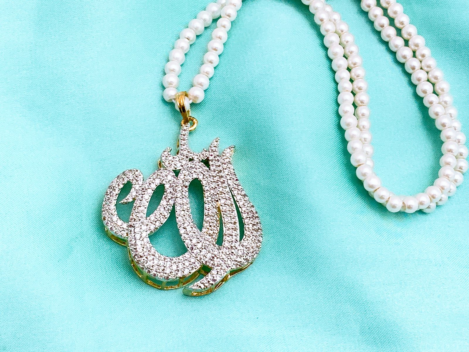 Silver Diamond Allah Calligraphy Pendant with Double-Strand Pearl Mala Diamond-encrusted silver Allah calligraphy pendant on a double-strand white pearl necklace, displayed on a light blue background.