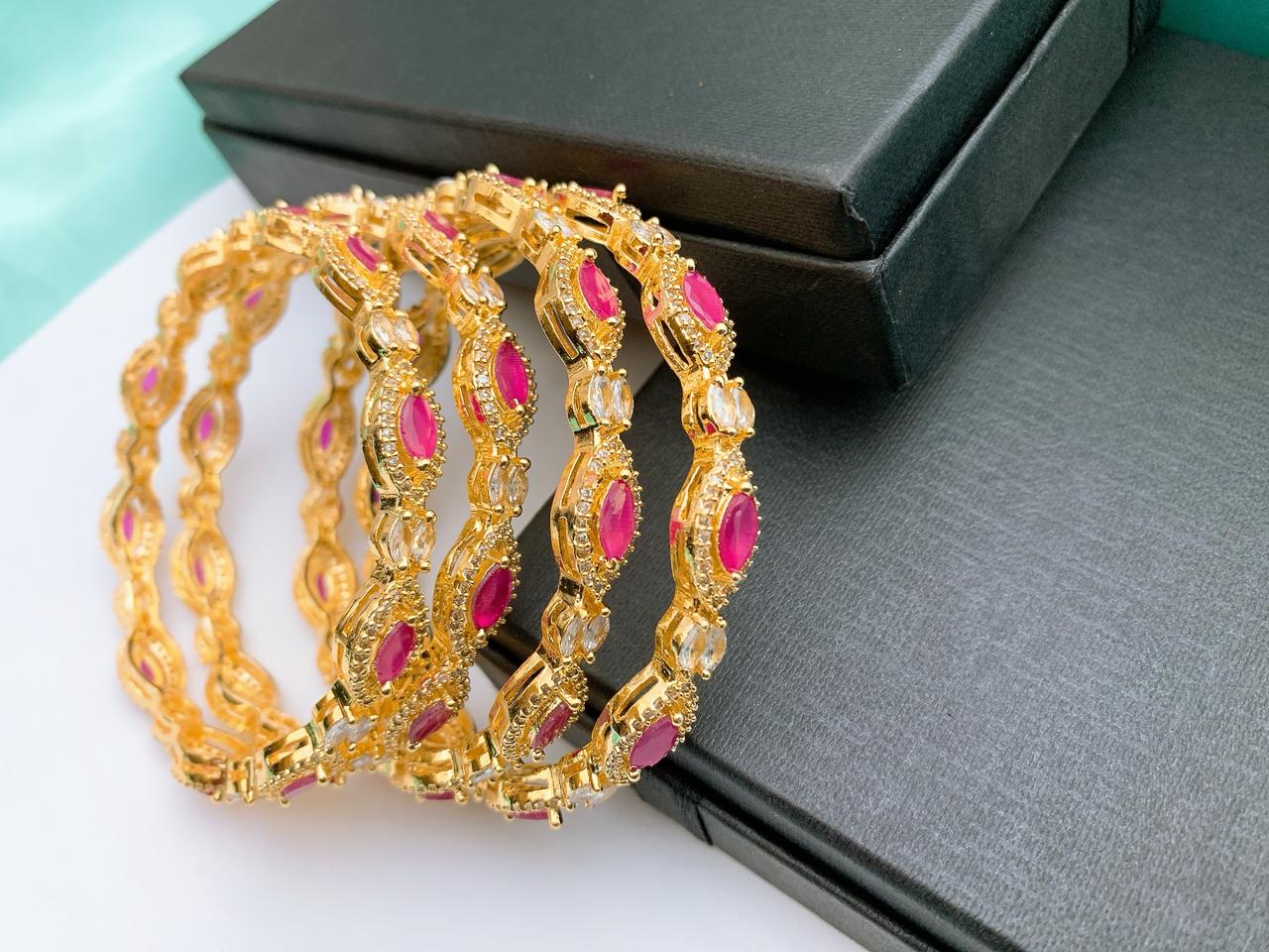 Gold plated American Diamond AD bangles set featuring ruby red stones and sparkling cubic zirconia accents, elegant bridal and party wear jewelry design for women in Italy. Elegant gold plated American Diamond bangles set designed for women in Italy. Featuring rich ruby red stones with brilliant AD sparkle, this stylish bridal and evening wear set offers sophisticated glamour for weddings, celebrations, and formal occasions. Lightweight, radiant, and perfect for festive styling.