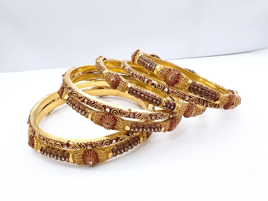 Set of seven premium 22ct gold-plated 1-gram bridal chooriyan bangles featuring radiating fan medallions, textured grid segments with red enamel, and clear rhinestone accents.