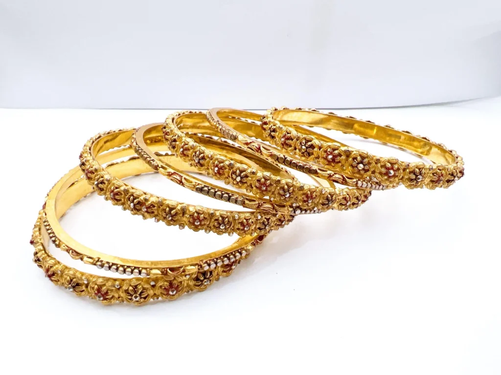 Set of seven premium 22ct gold-plated 1-gram bridal chooriyan bangles featuring raised antique floral medallions, maroon enamel accents, and textured micro-beaded borders.