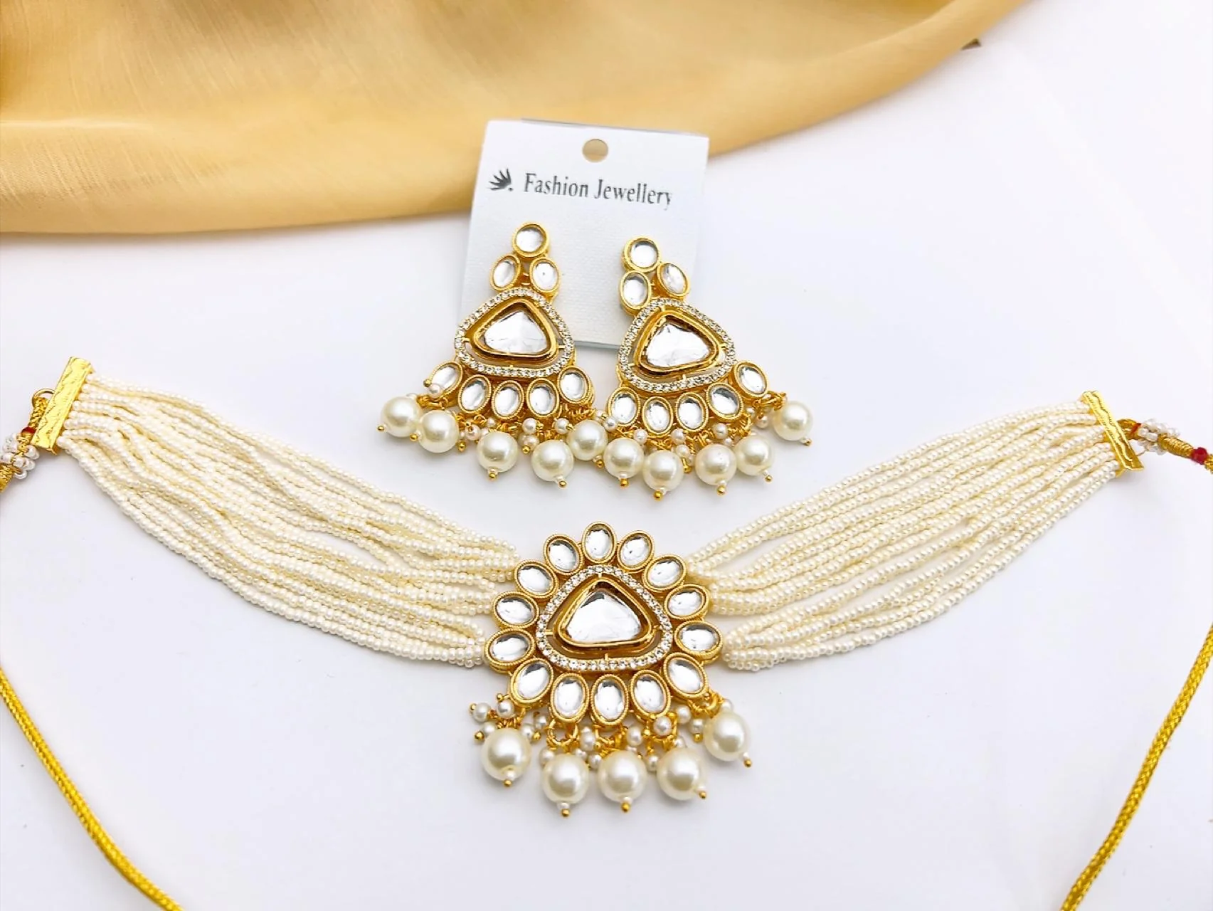 Premium White Kundan Choker Necklace Set with Drop Earrings Bring clean lines and dazzling reflection to your wardrobe. This gold-tone imitation choker stands out with its geometric square and rhombus-cut stone settings, beautifully framed by a uniform 12-strand faux pearl band and matching drop earrings.